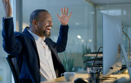 Black man, computer and celebration for promotion email, success and wow for bonus, happy smile and surprise in office. Businessman celebrate, surprise and happiness for good news or winner at night